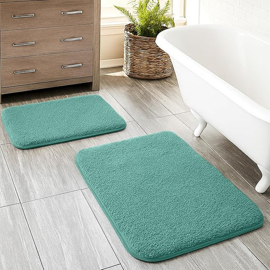 Set of two teal bathmats on a tiled bathroom floor beside a white bathtub and cabinet