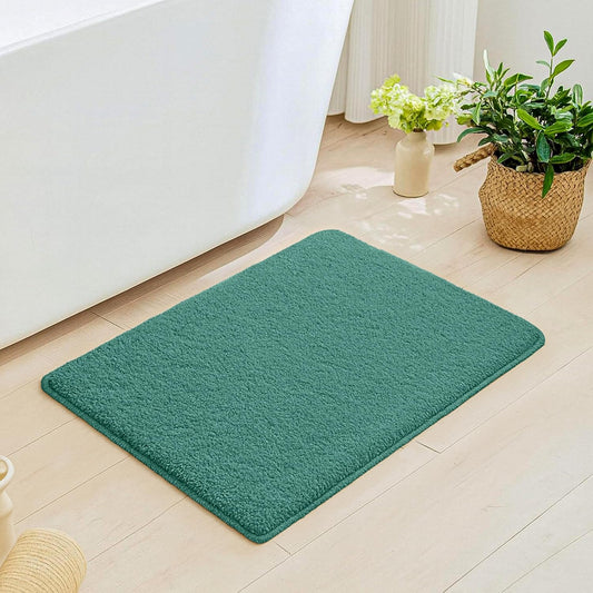 Green bathmat on light wood bathroom floor near white bathtub and potted plants