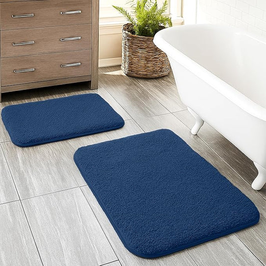 Set of two navy blue bathmats on bathroom tile floor near bathtub and wooden cabinet