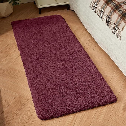 Plush maroon bathmat placed beside a bed on wooden flooring in a cozy bedroom.