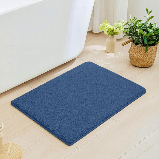 Blue bathmat on light wood bathroom floor near tub and potted plants