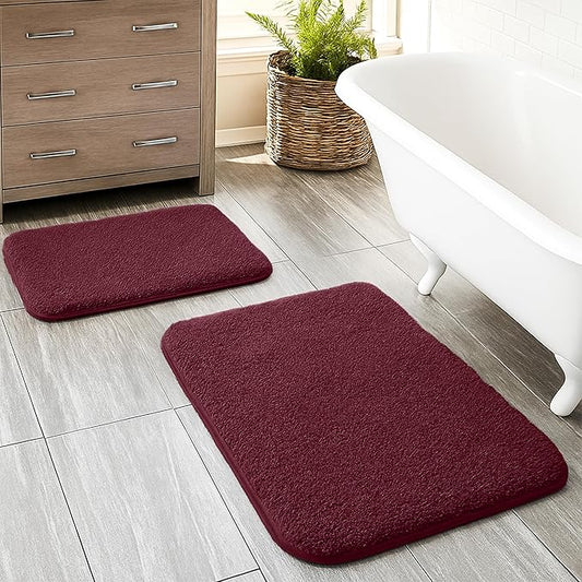 Set of two burgundy bathmats on bathroom floor near white bathtub and wooden cabinet