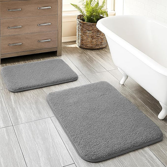 Two gray bathmats on a tiled bathroom floor near a bathtub and wooden cabinet