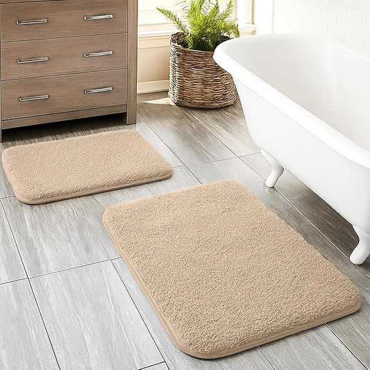 Beige bathmats on tiled bathroom floor near white bathtub and wooden cabinet