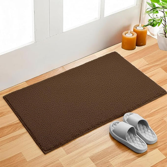 Brown bathmat on wooden floor by door with slippers, candles, and potted plant