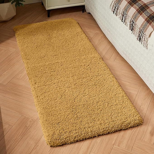 Soft yellow bathmat or bedroom runner rug on wooden floor beside a bed