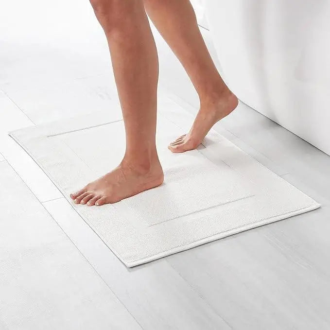 Person stepping on a white bathmat in a modern bathroom with light flooring