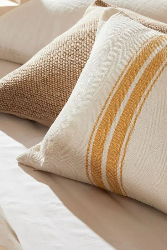 Decorative pillows on a neatly made bed with textured beige and striped cushion covers