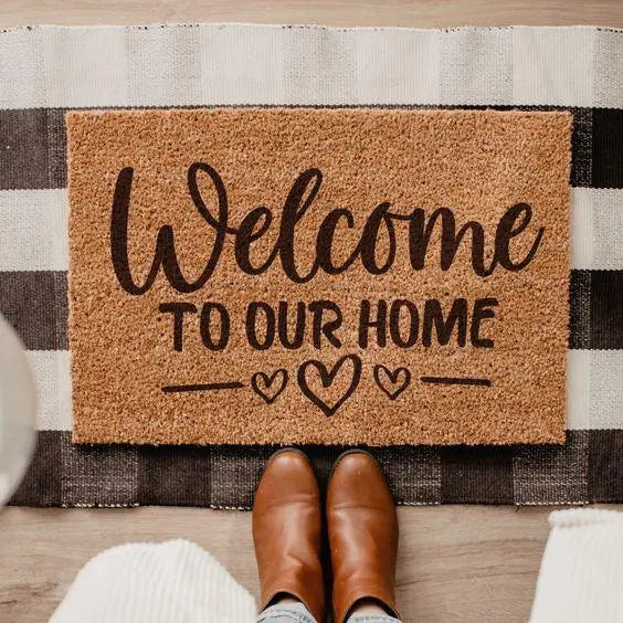 Coir welcome doormat with heart design on striped rug, brown boots in foreground