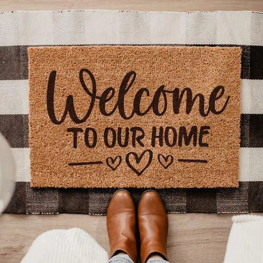 Coir welcome doormat with heart design on striped rug, brown boots in foreground