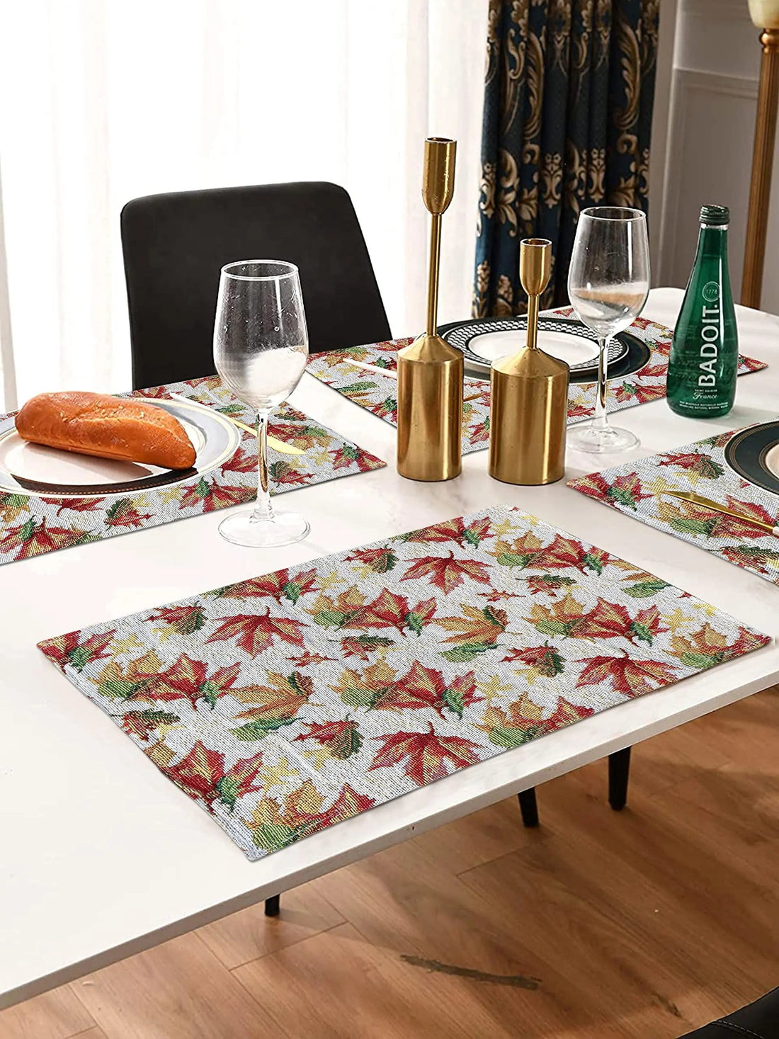 Dining table with autumn leaf print placemats, gold candle holders, and glassware