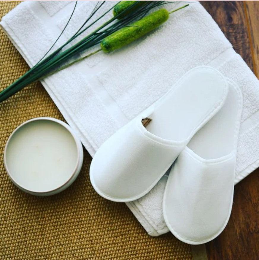 White slippers on folded towel with candle and green decor, bathroom essentials