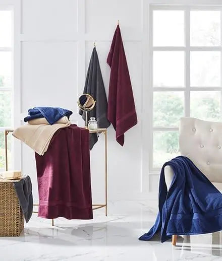 Assorted bath towels in navy blue, burgundy, beige, and grey in a modern bathroom setting.