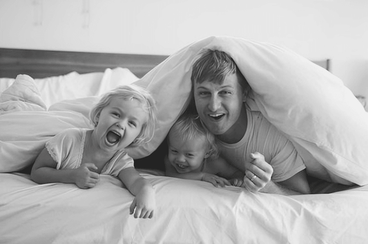 Family laughing under white comforter on bed, highlighting cozy bedding for bedrooms.