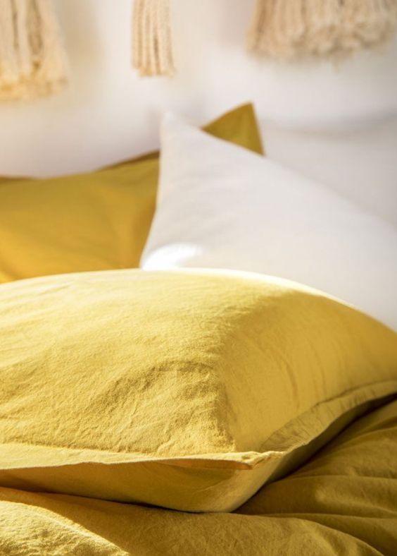 Yellow bedsheet and pillow set with a white accent pillow on a cozy bed