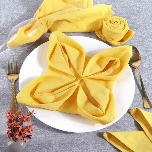 Yellow cotton napkin folded flower-shaped on white plate, gold cutlery, elegant table setting