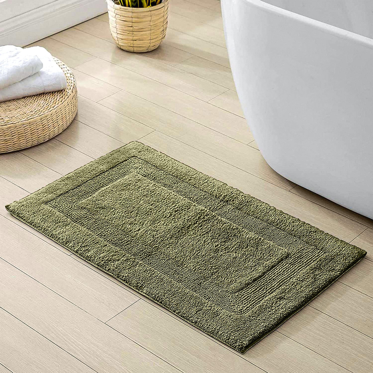 Green bathmat on light wood bathroom floor beside bathtub and woven basket.