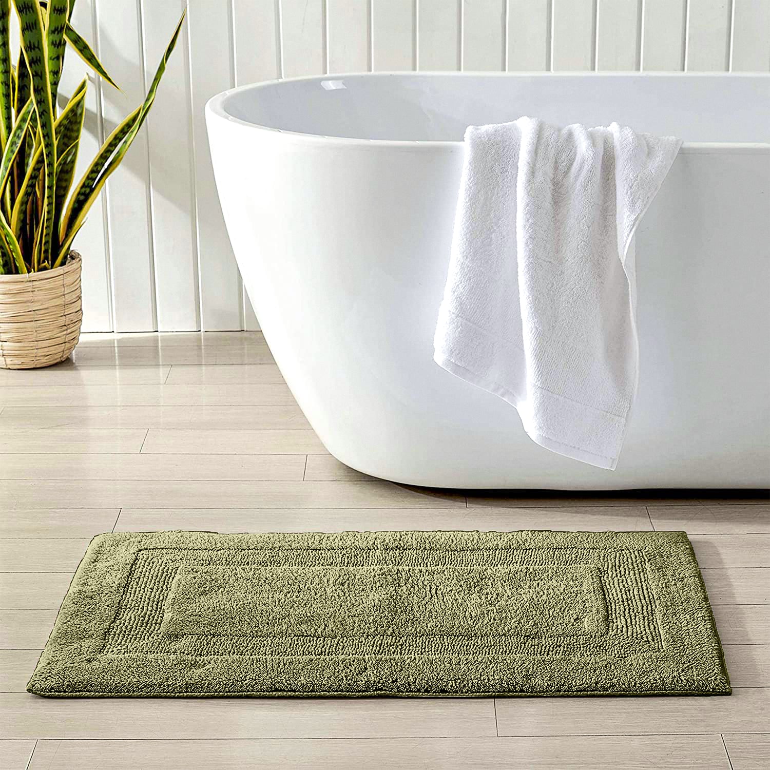 Green bathmat near white bathtub with towel, potted plant, and wooden floor