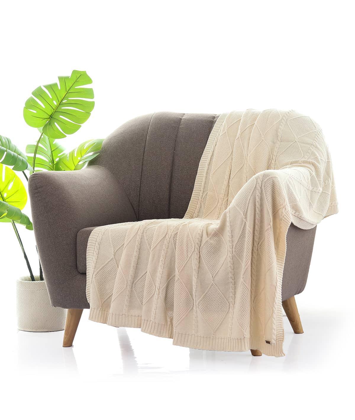 Beige knitted throw blanket draped over a modern grey armchair beside a potted green plant