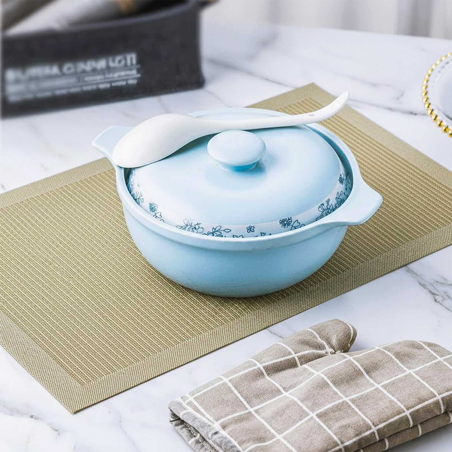 Light blue ceramic casserole dish with floral pattern and white serving spoon on placemat