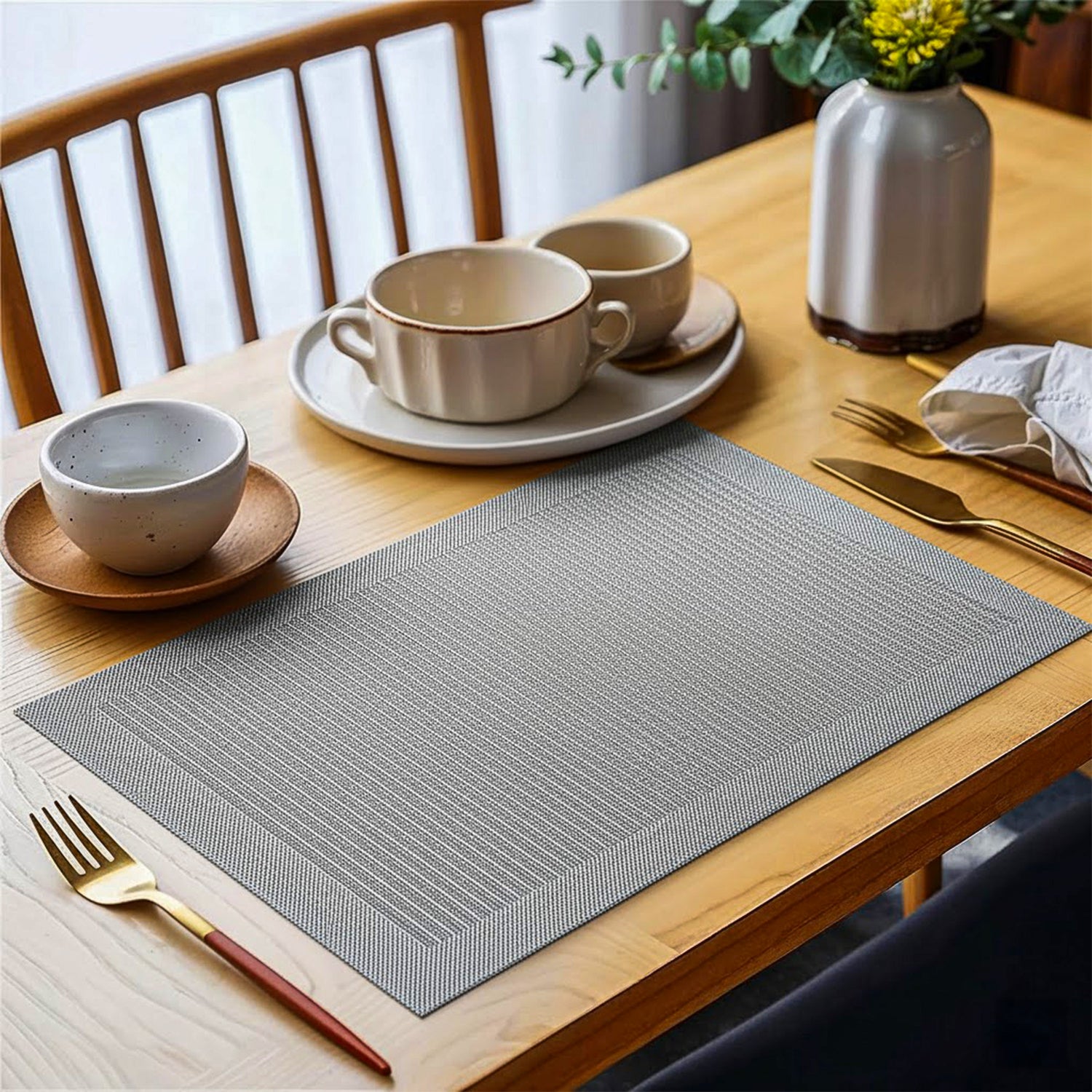 Textured grey placemat on dining table with ceramic cups, plates, and gold cutlery