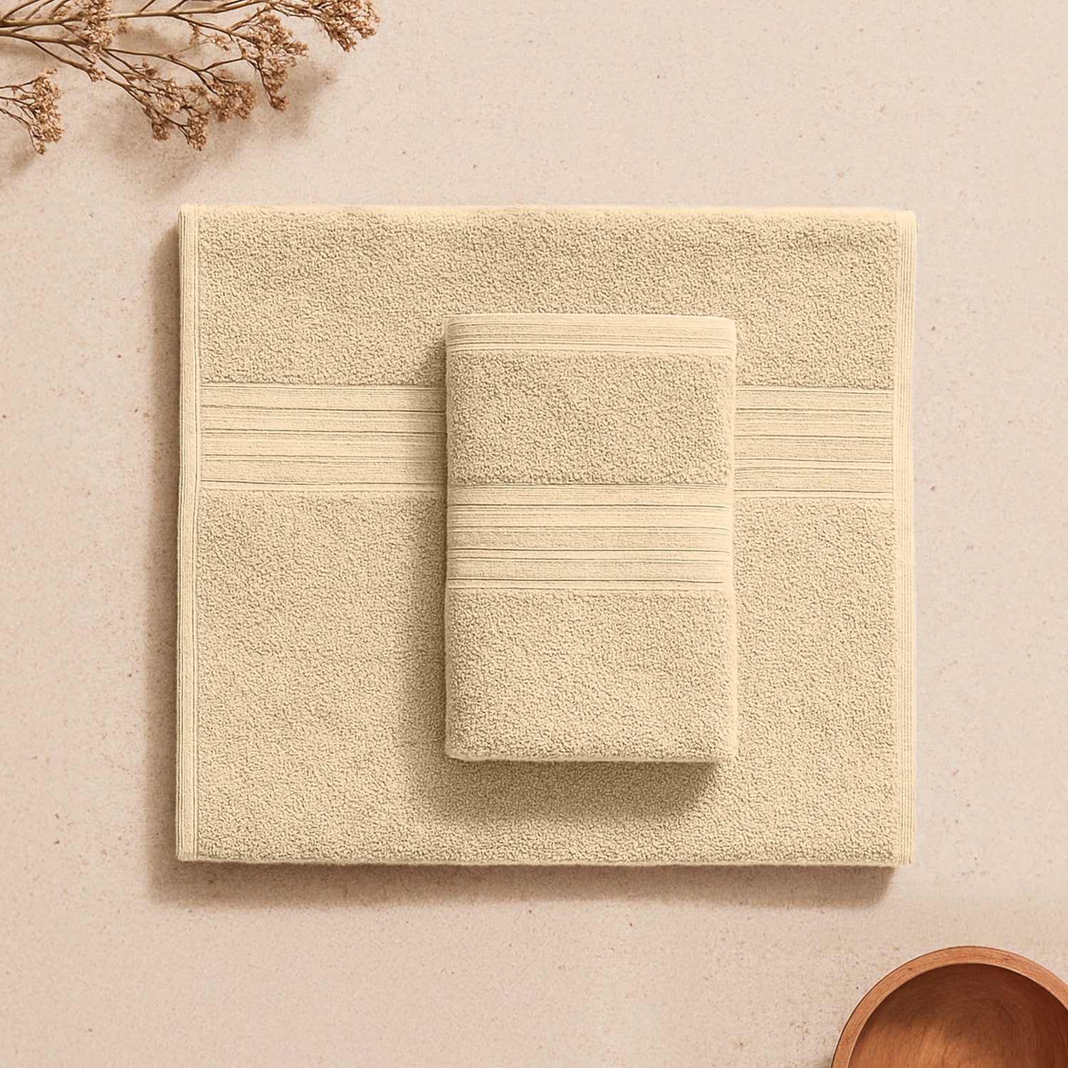 Beige cotton towel set neatly folded on a cream surface with subtle dried plant decor.