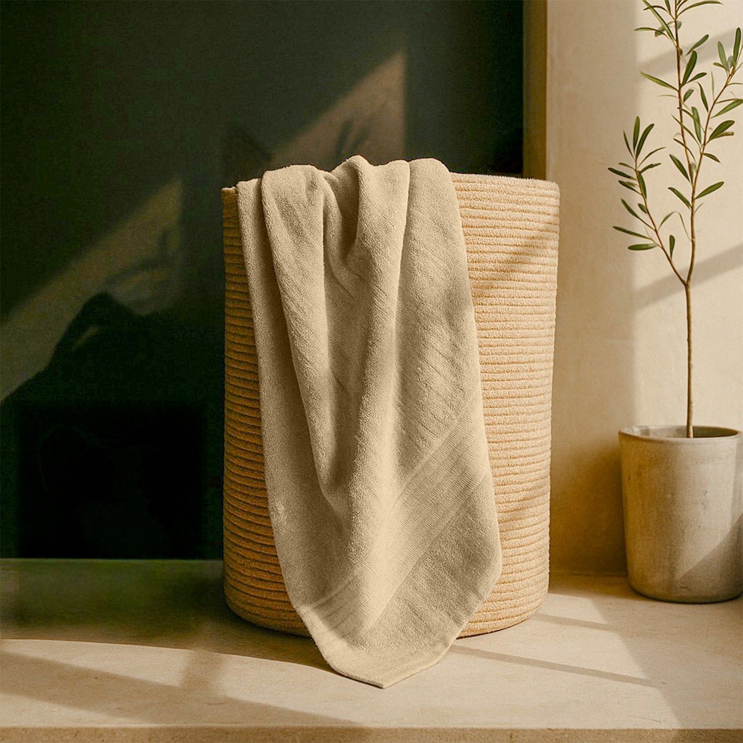 Beige cotton bath towel draped over woven laundry basket near potted plant in natural light