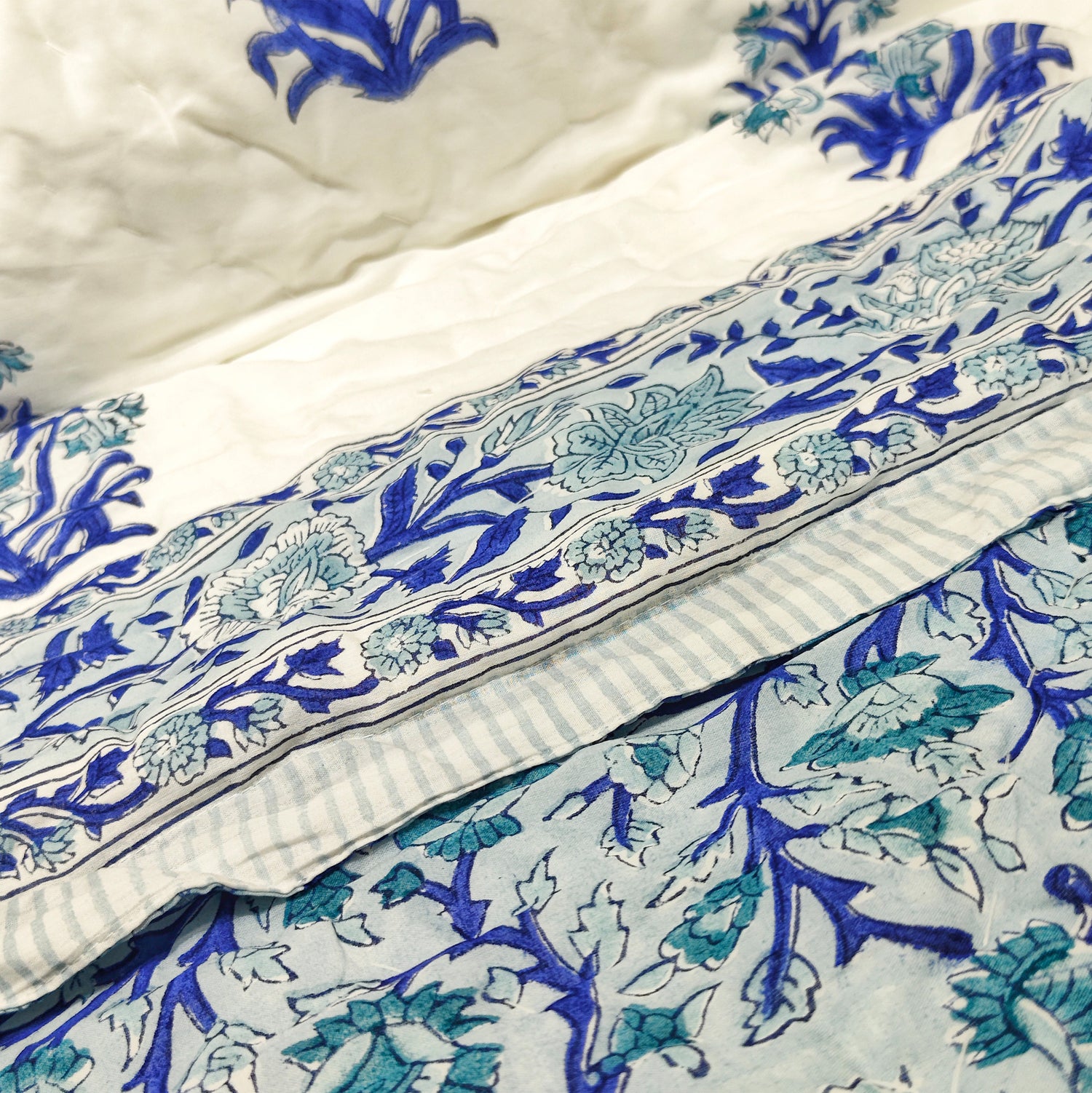 Blue floral printed quilt with striped edging on a bed, soft cotton fabric