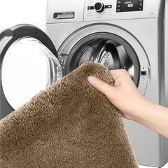 Hand holding soft brown bathmat in front of washing machine, washable bathroom rug