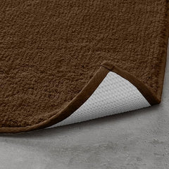 Brown textured bathmat with non-slip white backing on a grey floor