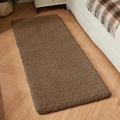 Brown rectangular bathmat or area rug on wooden floor beside a bed.