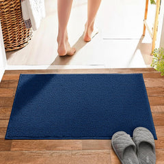 Blue bathmat on wooden floor with grey slippers and a person standing nearby