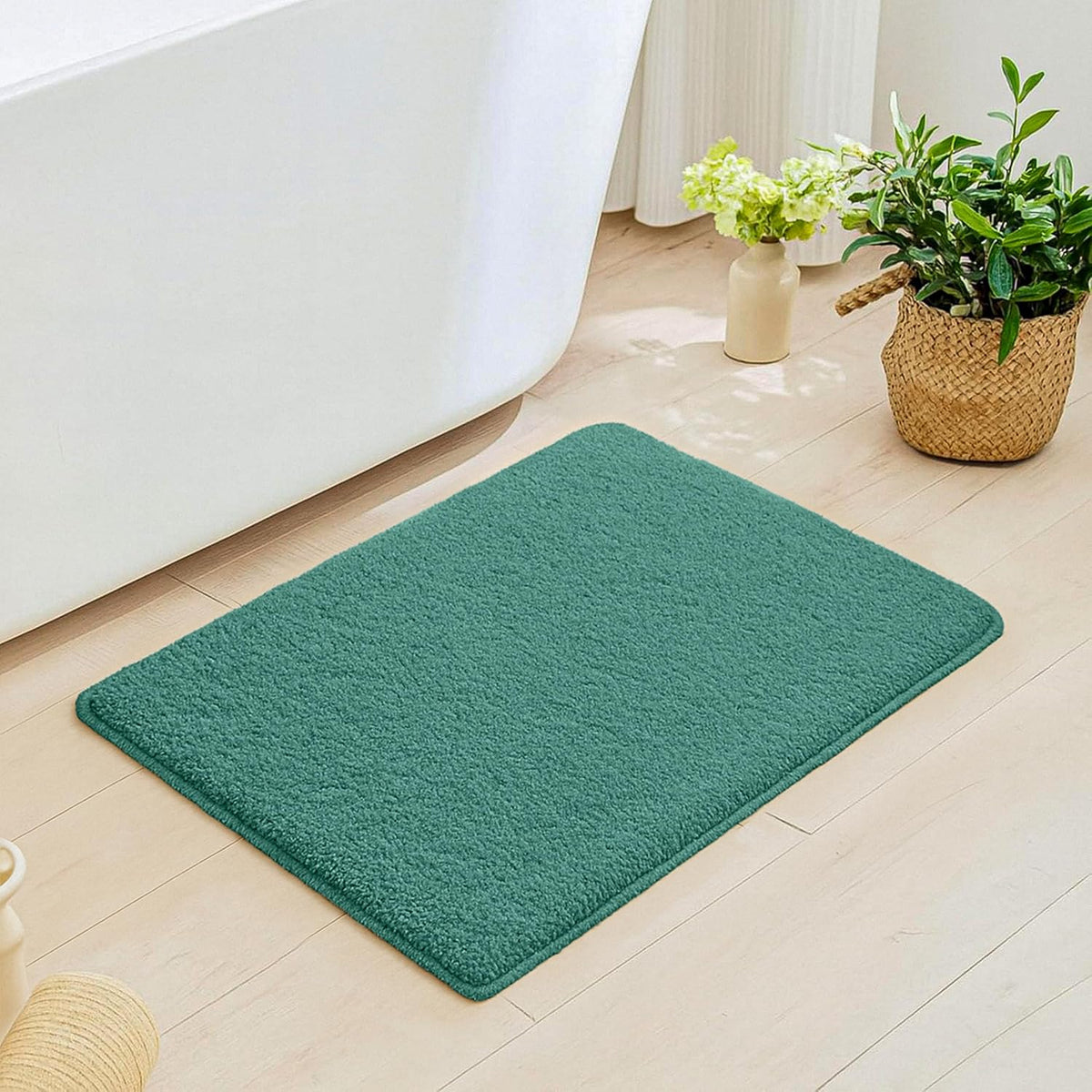 Green bathmat on light wood bathroom floor near white bathtub and potted plants