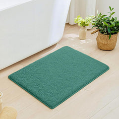 Green bathmat on light wood bathroom floor near white bathtub and potted plants
