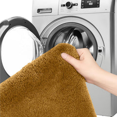Hand holding a brown bathmat in front of a washing machine, showing easy washable home essentials.
