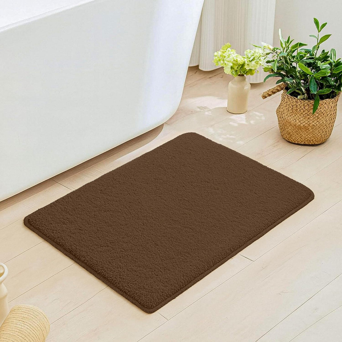 Brown bathmat on light bathroom floor near bathtub and indoor plants