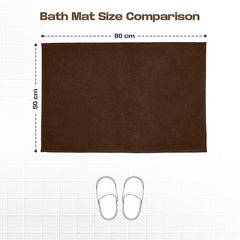 Brown bath mat 50x80 cm on white tiles with size comparison to slippers.