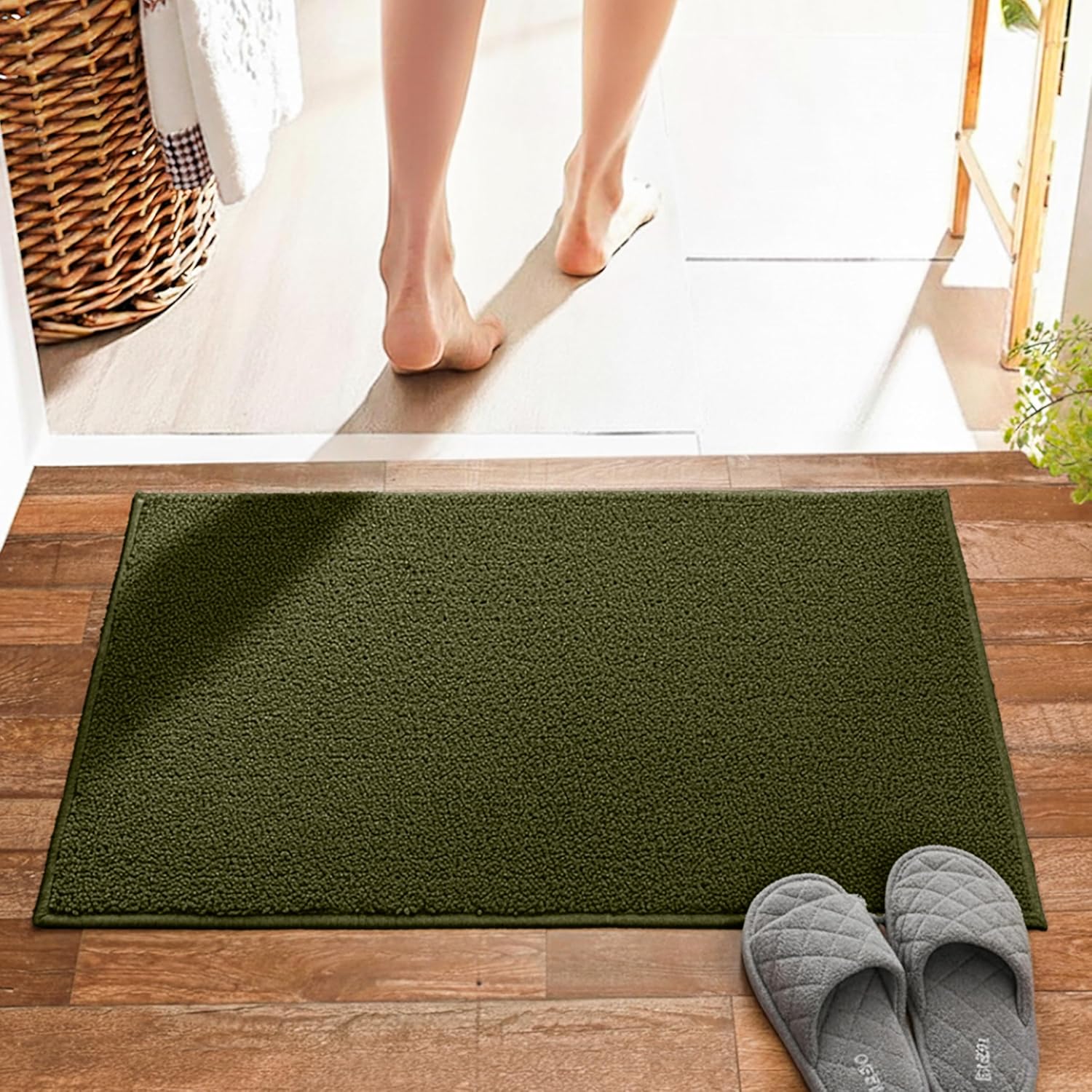 Green bath mat on wooden floor with gray slippers, feet stepping out of bathroom
