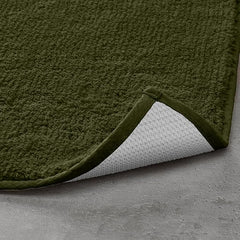 Olive green bathmat with non-slip backing on a grey floor