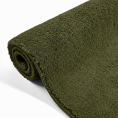 Rolled dark green bathmat with soft textured surface on white background