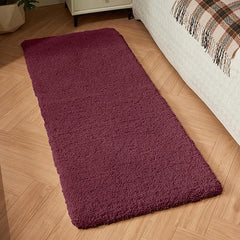 Plush maroon bathmat placed beside a bed on wooden flooring in a cozy bedroom.
