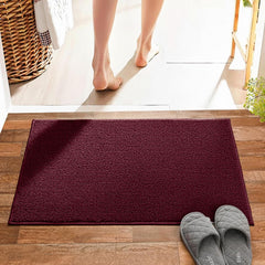 Burgundy bathmat on wood floor with gray slippers and person stepping out of bathroom