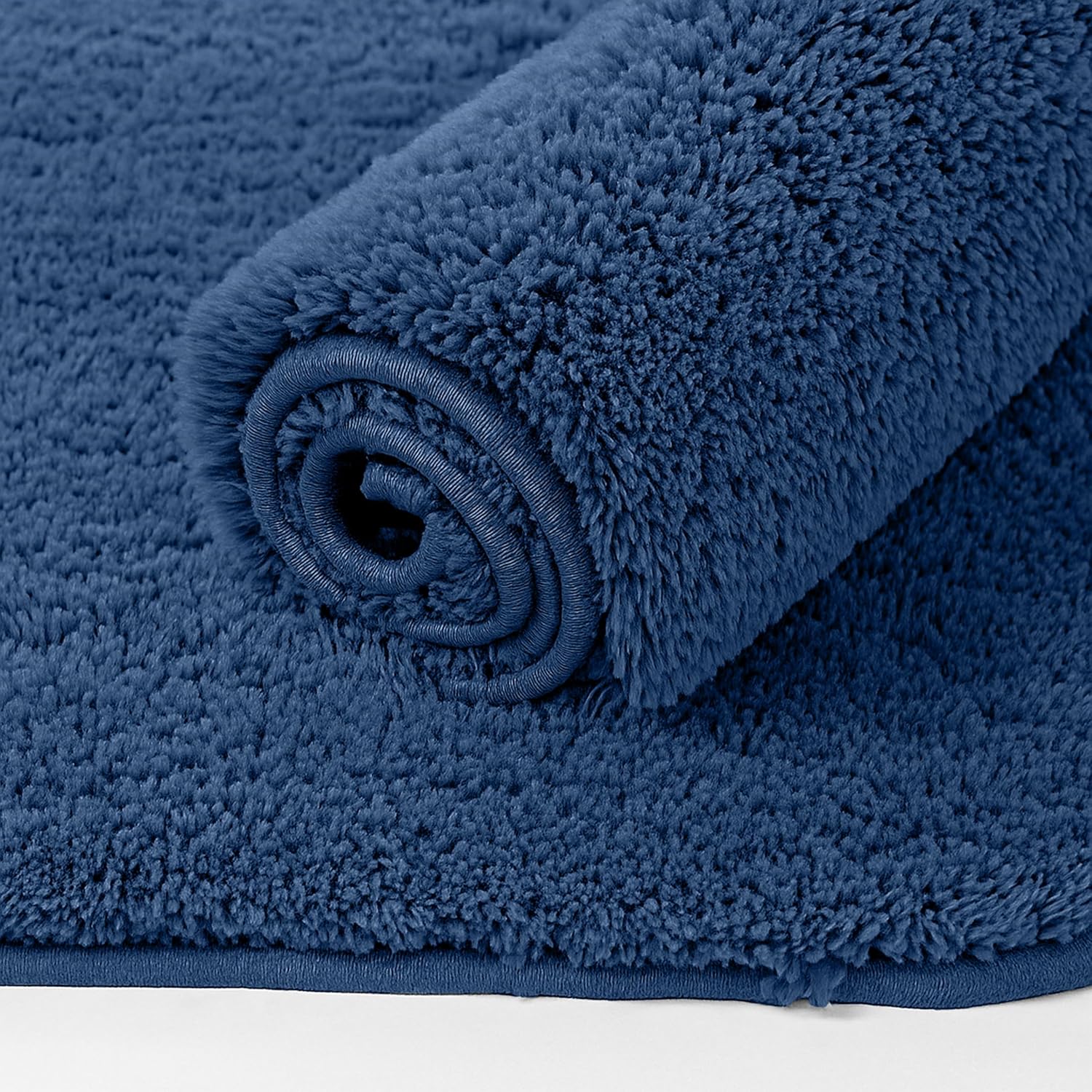 Fluffy dark blue bathmat rolled up on a white background, soft bathroom rug