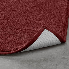 Red textured bathmat with non-slip backing on a grey floor