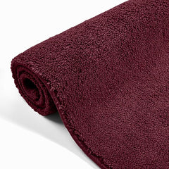 Rolled maroon bathmat with soft textured surface on white background