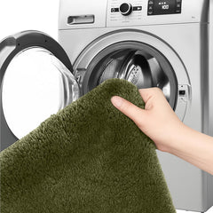 Hand holding a green fluffy bathmat near a front-loading washing machine