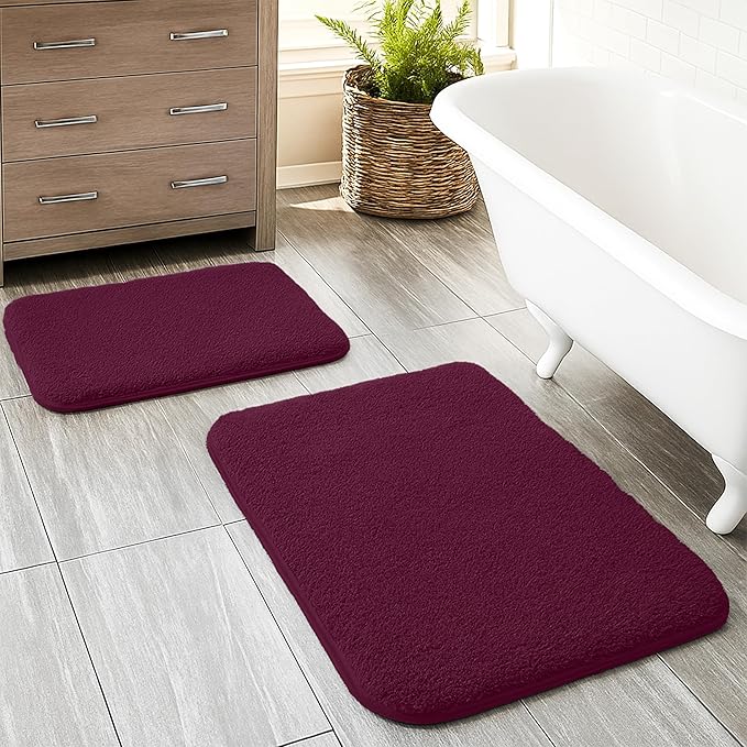 Set of two maroon bathmats on bathroom tile floor beside a white bathtub