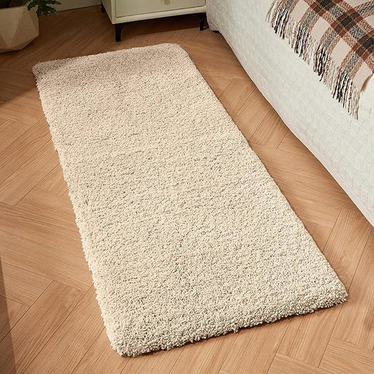 Beige rectangular bathmat on wooden floor beside a bed with plaid blanket