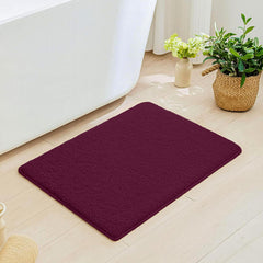 Plush maroon bathmat on light wood floor next to white bathtub with plants nearby