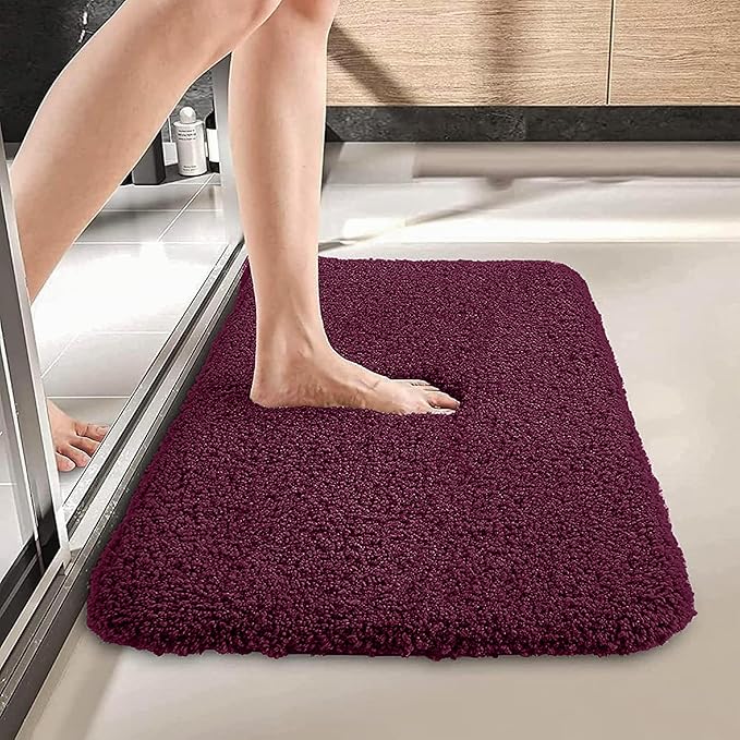 Plush maroon bathmat in bathroom with foot stepping out of shower onto soft surface